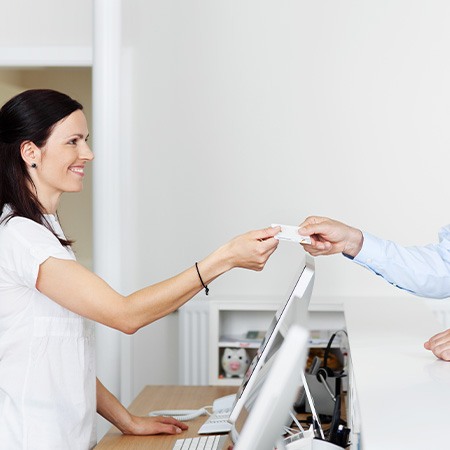 Smiling patient handing dental assistant credit card