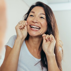 Woman smiling while flossing her teeth in bathroom