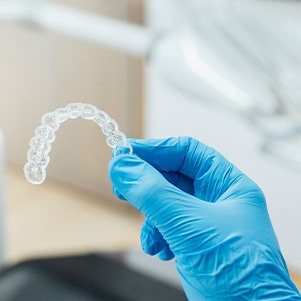 Dentist with blue gloves holding clear aligner