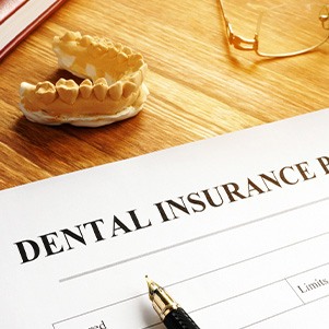 A dental insurance form next to some glasses and a jaw model