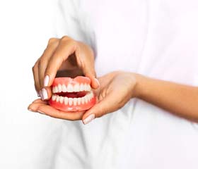 Close up of woman holding upper and lower dentures