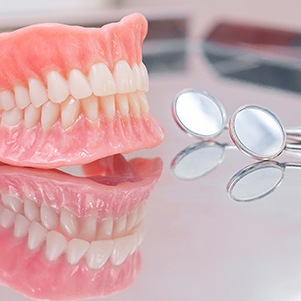 Full dentures sitting on reflective surface next to dental mirrors