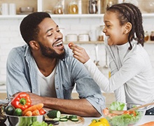 little girl giving her dad a cherry tomato