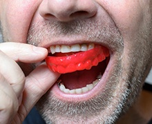 man putting a red mouthguard into his mouth 