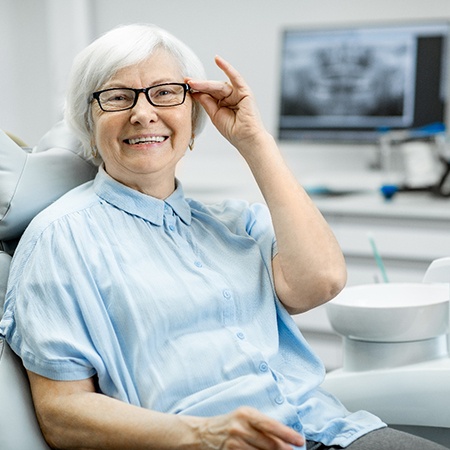 Senior woman in dental chair smiling and adjusting her glasses