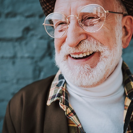 Senior man with glasses smiling in front of brick wall