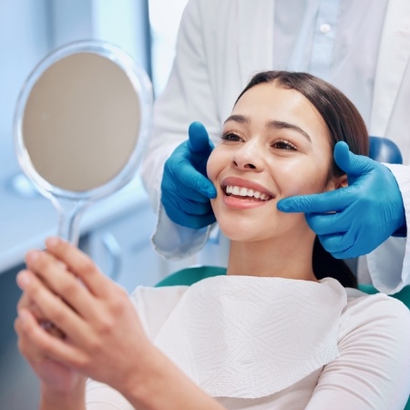 Woman checking teeth in mirror after smile makeover