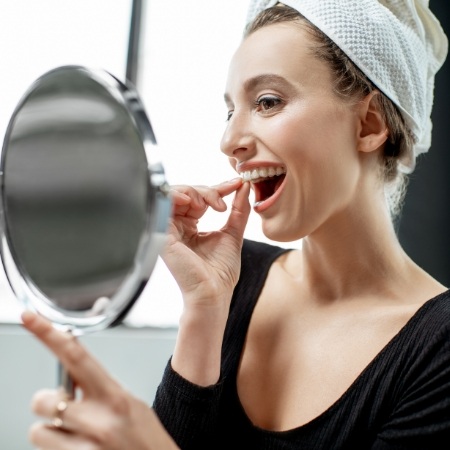 Woman wearing whitening tray checking smile in mirror