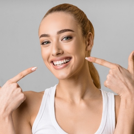 Woman in white shirt pointing to her smile